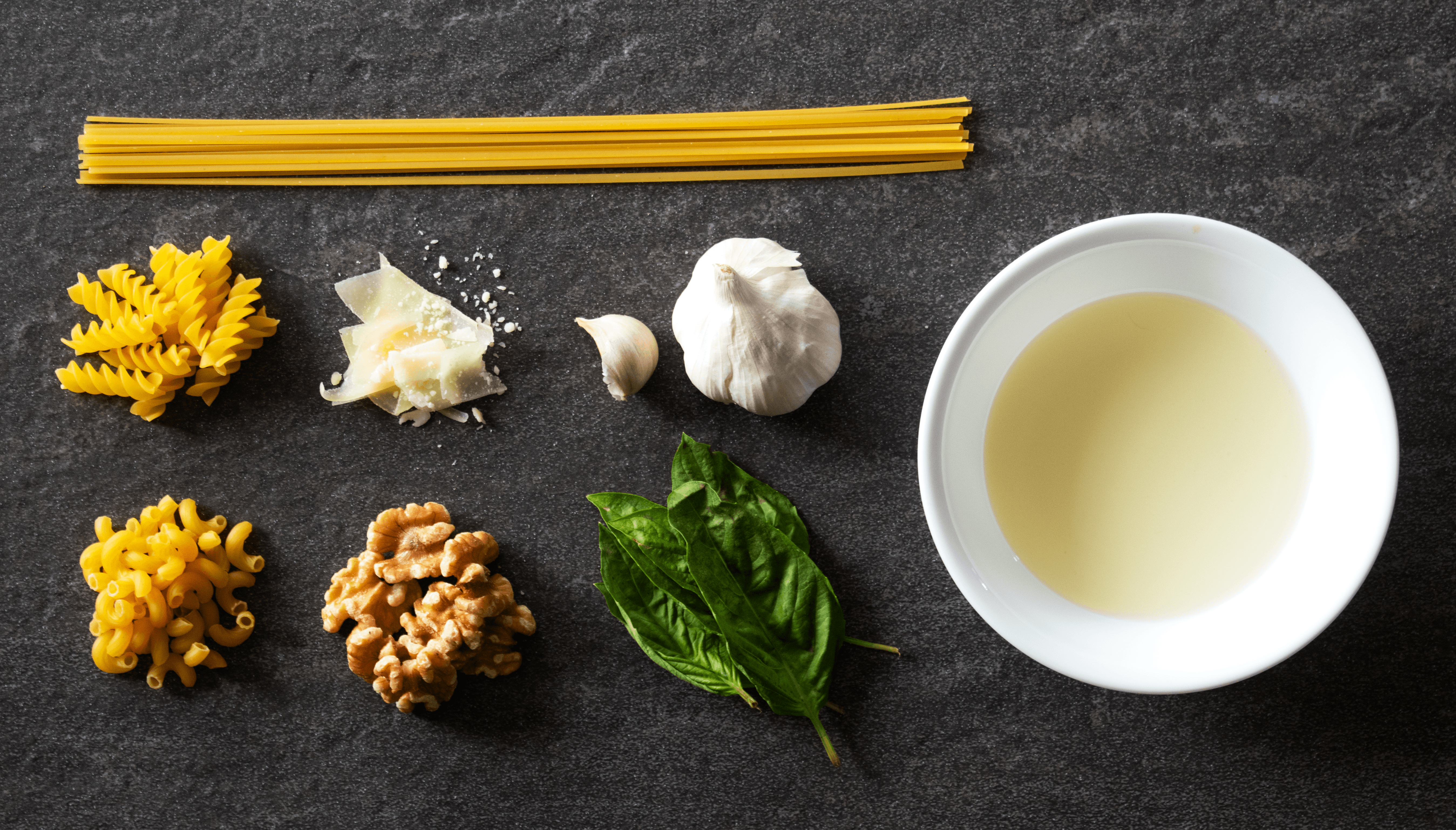 On a black surface there are ingridents for the pesto used in the recipe